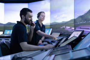 An ATC trainee and instructor in the Tower SIM against a simulated sky and trees